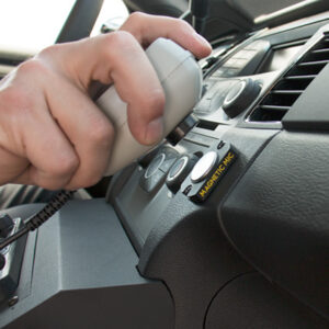 Hand placing a two-way radio microphone onto a Magnetic Mic mount on a vehicle dashboard.